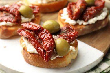 Krem peynirli lezzetli bruschettalar, güneşte kurutulmuş domatesler ve yeşil zeytinler masada, yakın plan.