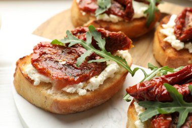 Krem peynirli lezzetli bruschettalar, güneşte kurutulmuş domatesler ve masanda roka, yakın plan.