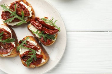 Krem peynirli nefis bruschettalar, güneşte kurutulmuş domatesler ve beyaz ahşap masa üzerinde roka, üst manzara. Metin için boşluk