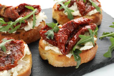 Krem peynirli lezzetli bruschettalar, güneşte kurutulmuş domatesler ve masanda roka, yakın plan.