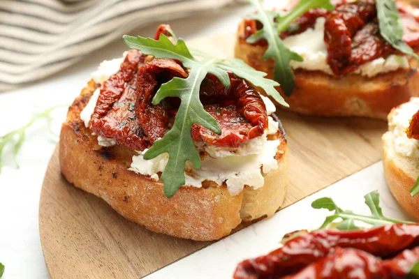 Krem peynirli lezzetli bruschettalar, güneşte kurutulmuş domatesler ve masanda roka, yakın plan.