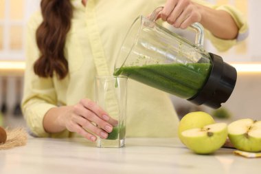 Kadın, beyaz mermer masada, blenderdan cama leziz bir smoothie dolduruyor.