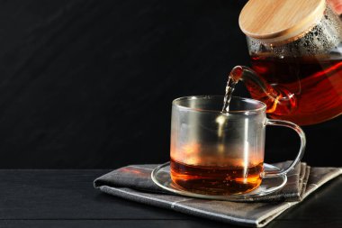 Siyah ahşap masada çaydanlıktan fincana sıcak çay dolduran kadın, yakın plan. Metin için boşluk