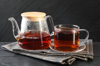 Sıcak çay fincanda ve çaydanlık siyah ahşap masada.