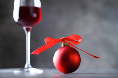 Bir kadeh kırmızı şarap ve Noel mücevheri gri masada, yakın plan.