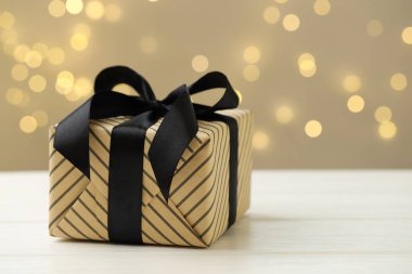 Bulanık ışıklara karşı beyaz ahşap masaya güzelce sarılmış bir hediye, yakın plan. Metin için boşluk