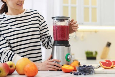 Gülümseyen kadın mutfaktaki beyaz mermer masada blender ile leziz bir smoothie yapıyor.