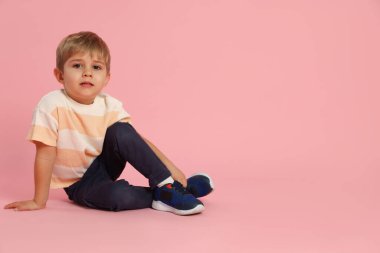 Pembe arka planda oturan sevimli küçük çocuk. Metin için boşluk