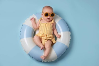 Şişirilebilir halkada güneş gözlüklü şirin bir bebek açık mavi arka planda, üst tarafta.