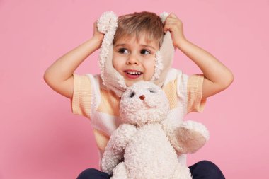 Pembe arka planda oyuncak tavşanı olan küçük mutlu çocuk.