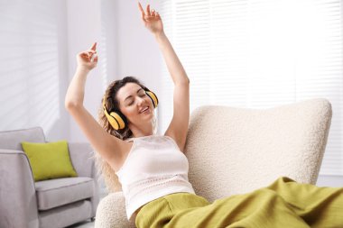 Kulaklıklı mutlu kadın evdeki koltukta müzik dinliyor.