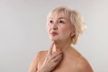 Üst düzey kadın açık gri arka planda boynuna dokunuyor. Metin için boşluk