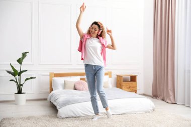 Kulaklıklı gülümseyen kadın yatak odasında dans ediyor.