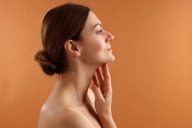 Güzel bir kadın soluk turuncu arka planda boynuna dokunuyor.