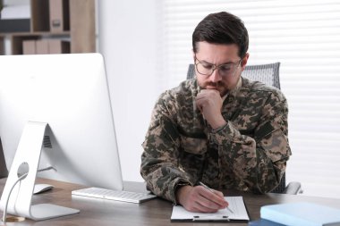 Askeri eğitim. Asker üniforması içindeki öğrenci ahşap masada öğreniyor.