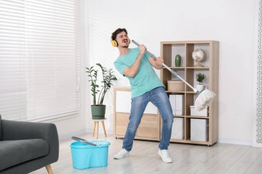 Evde temizlik yaparken, kulaklıklı mutlu bir adam şarkı söylüyor.