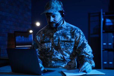 Askerlik. Kulaklıklı bir asker, gece ofiste ahşap masada çalışıyor.