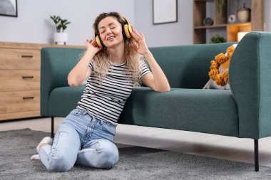 Kulaklıklı mutlu kadın evdeki kanepenin yanında müzik dinliyor.
