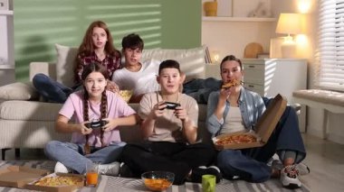 Video oyunu oynayan ve evde abur cubur yiyen bir grup genç.