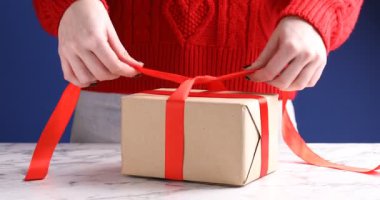 Beyaz mermer masada, mavi arka planda, noel hediyesine yay bağlayan kadın, yakın plan