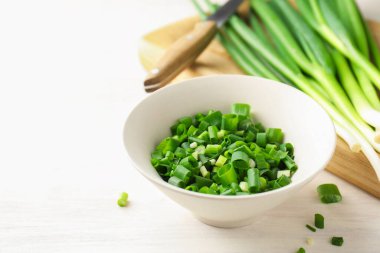 Beyaz ahşap masada yeşil soğanları kaseye koy, yakın plan. Metin için boşluk