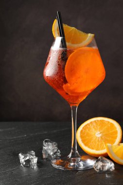 Bir bardak ferahlatıcı spritzer kokteyli, buz küpleri ve siyah masada portakal dilimleri.