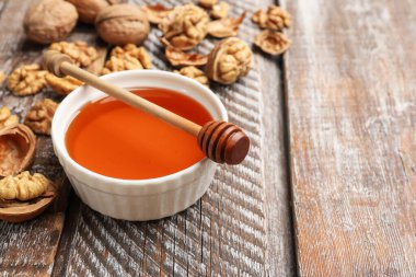 Honey in bowl, walnuts and dipper on wooden table, closeup. Space for text