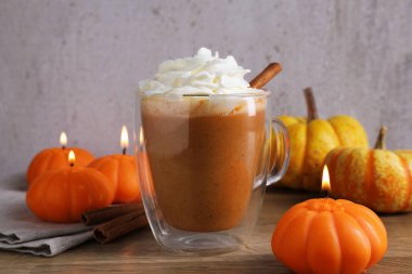 Cam bardakta kremalı balkabaklı latte, tarçın çubukları, taze sebzeler ve ahşap masada yanan mumlar, yakın plan.