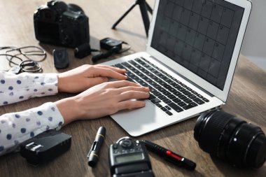 Ahşap masada dizüstü bilgisayarı, kamerası ve diğer ekipmanları olan profesyonel fotoğrafçı, yakın plan.