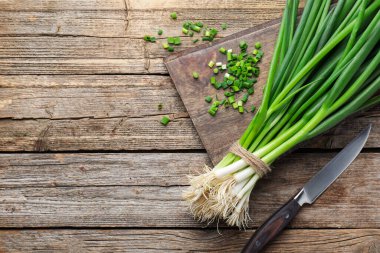 Fresh ripe green onions and knife on wooden table, top view. Space for text