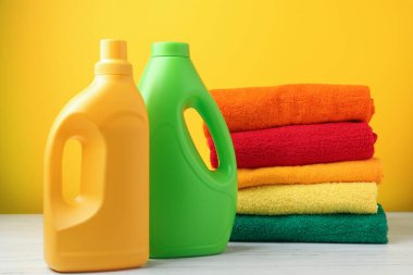 Çamaşır ve deterjan şişeleri beyaz ahşap masada, sarı arka planda, yakın plan.