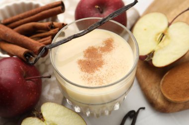 Lezzetli protein karışımı cam, elma, tarçın ve vanilya kabukları beyaz masada, yakın plan.