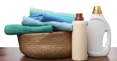 Çamaşır sepetinde havlular ve beyaz arka plandaki ahşap masada duran deterjan şişeleri.