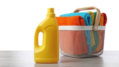 Çamaşır sepetinde havlular ve bir şişe deterjan beyaz arka plana karşı ahşap masada.