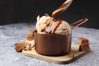 Gri masadaki bademli lezzetli dondurmanın üzerine karamel sosu dök.