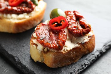 Krem peynirli lezzetli bruschettalar, güneşte kurutulmuş domatesler, kırmızı biber ve yeşil zeytinler masada, yakın plan.