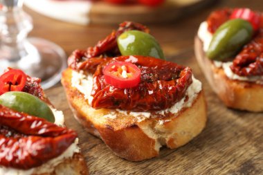 Krem peynirli lezzetli bruschettalar, güneşte kurutulmuş domatesler, kırmızı biber ve ahşap masada yeşil zeytinler, yakın plan.