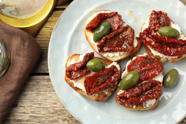 Krem peynirli lezzetli bruschettalar, güneşte kurutulmuş domatesler ve ahşap masada yeşil zeytinler.