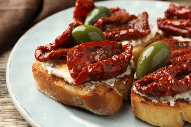 Krem peynirli lezzetli bruschettalar, güneşte kurutulmuş domatesler ve yeşil zeytinler masada, yakın plan.