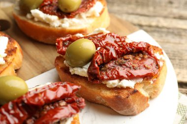 Krem peynirli lezzetli bruschettalar, güneşte kurutulmuş domatesler ve yeşil zeytinler masada, yakın plan.