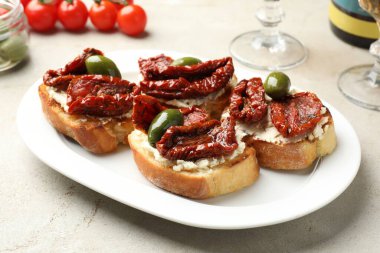 Krem peynirli lezzetli bruschettalar, güneşte kurutulmuş domatesler ve gri masada yeşil zeytinler, yakın plan.