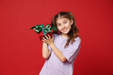 Kırmızı arka planda hediye kutusuyla gülümseyen kız.