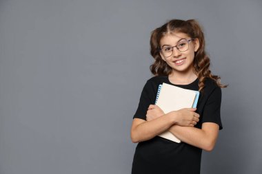 Gri arkaplan üzerine kitabı olan gözlüklü gülümseyen kız. Metin için boşluk