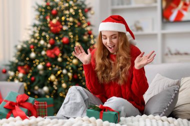 Noel Baba şapkalı duygusal bir kadın koltukta Noel hediyeleriyle rahat odasındaki bulanık ışıklara karşı. Metin için boşluk