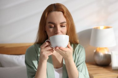 Evdeki yatakta kahve içen güzel bir kadın.