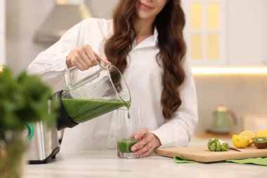 Kadın, beyaz mermer masada, blenderdan cama leziz bir smoothie dolduruyor.