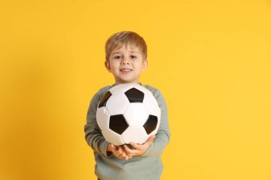 Sarı arka planda futbol topu olan sevimli küçük bir çocuğun portresi.