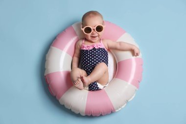 Şişirilebilir halkada güneş gözlüklü şirin bir bebek açık mavi arka planda, üst tarafta.