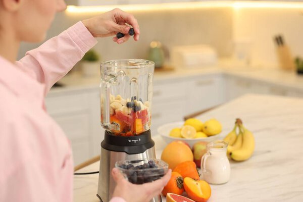 Woman making delicious smoothie with blender at white marble table in kitchen, closeup