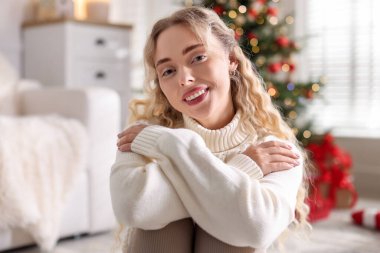 Evdeki bulanık ışıklara karşı süveter giymiş gülümseyen kadın portresi. Mutlu Noeller ve mutlu yıllar.